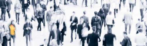 Uklart fotografi av en menneskemengde i en travel gate. Bildet er tatt skrått ovenfra, i fugleperspektiv, og vi ser mest ryggene til en mengde voksne mennesker. Fotoet er i lyse gråtoner.