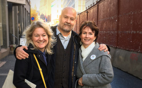 Foto av tre voksne personer som ser inn i kameraet og smiler. Fra venstre: En kvinne med blondt hår og sort jakke, en mann med skjeogg, skjorte og genser og en kvinne med kort, brunt hår, grå jakke og hvitt skjerf.
