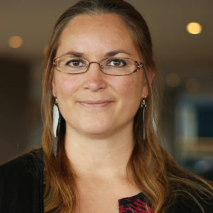 Fotografi av Siri Kristine Engstad. Fotografiet er fra skuldrene og opp. En kvinne med mellomlangt, brunt hår, briller og brune øyne smiler og ser rett i kameraet. Bakgrunnen er uklar.